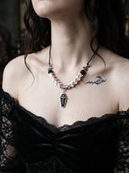 Coffin Oath Snake Bone Necklace, front view of coffin charm and pale snake bone necklace on a model in black