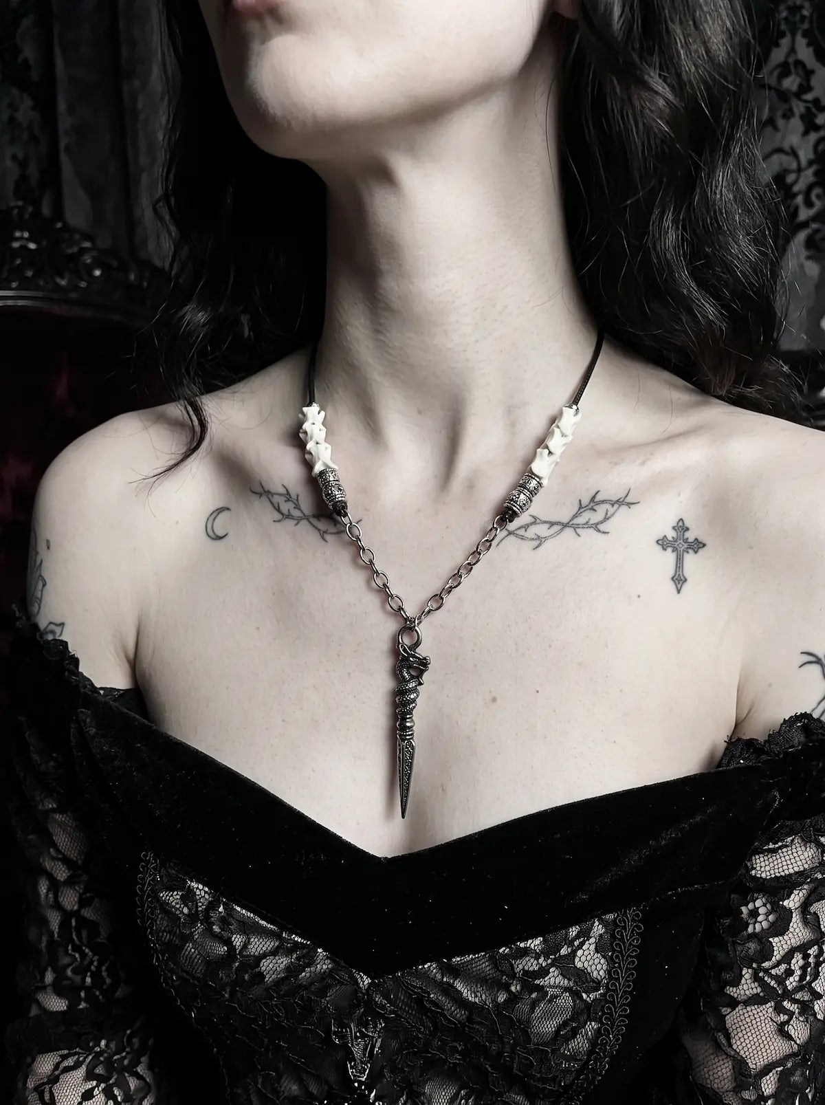 Coilblade Snake Bone Necklace, side chest view of a long silver-tone blade hanging from a pale bone necklace