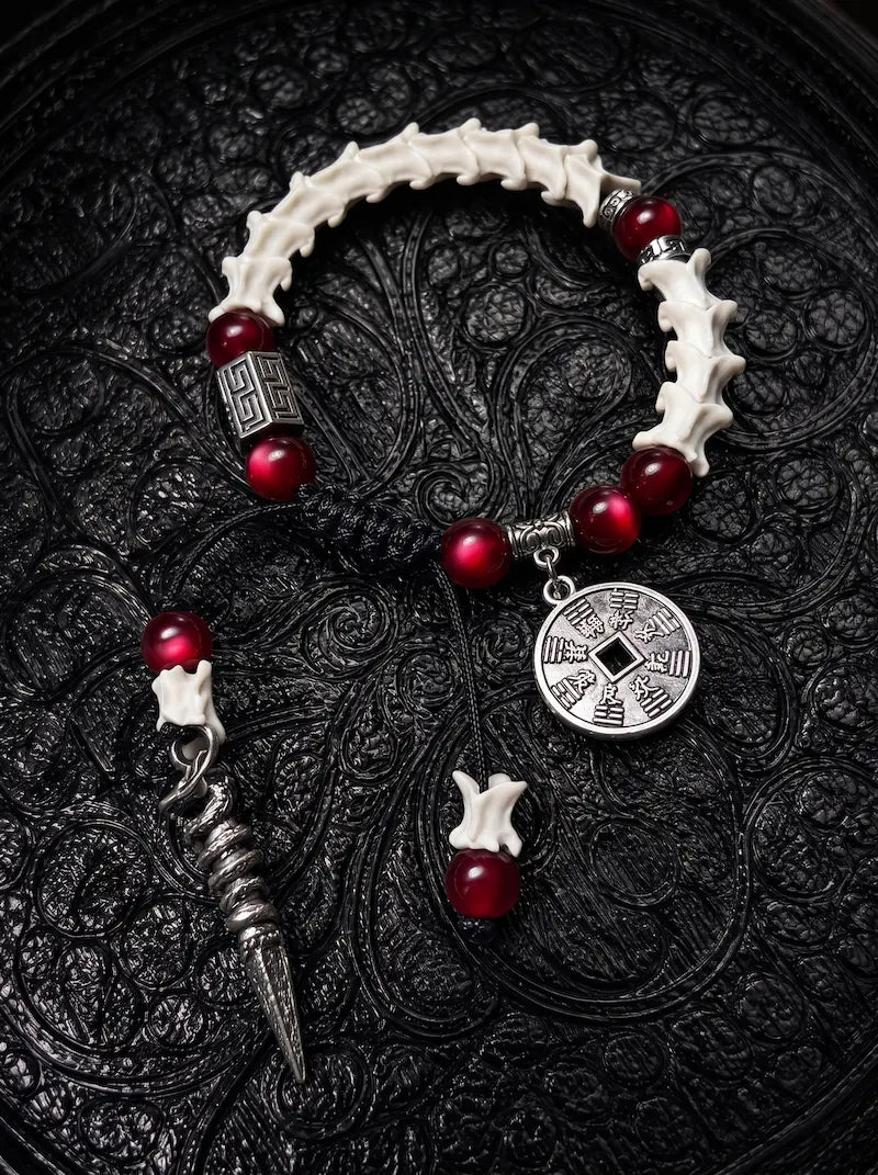 Crimson Coin snake bone bracelet with deep red beads, an engraved round coin and a long pointed metal drop on black cords