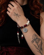 Crimson Coin snake bone bracelet worn with the hand at the collarbone, showing its coin charm and long pointed drop