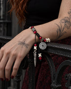 Crimson Coin snake bone bracelet on a hand resting over a dark railing, with the coin and pointed pendant hanging down