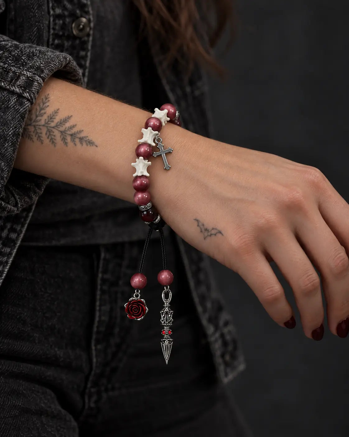 Crimson Cross snake bone bracelet on a wrist resting across the lap, with its cross and long cord ends visible