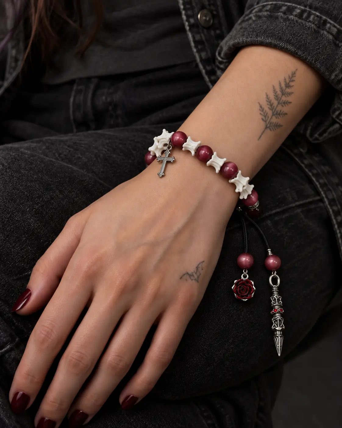 Crimson Cross snake bone bracelet on a hand resting on black jeans, showing the cross beside white vertebrae