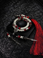 Crimson Lotus double-wrap snake bone bracelet with red beads, a lotus charm and pointed metal drops, beside a red tassel