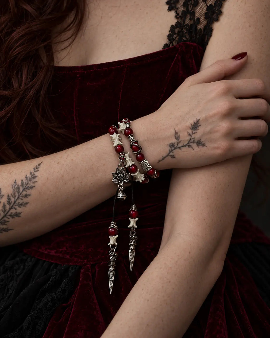 Crimson Lotus double-wrap snake bone bracelet worn with the hand resting on the opposite upper arm above burgundy velvet
