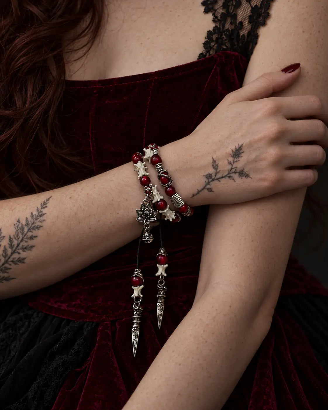 Crimson Lotus double-wrap snake bone bracelet worn with the hand resting on the opposite upper arm above burgundy velvet