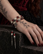 Crimson Lotus snake bone bracelet on a wrist resting on a stone ledge, with two long pointed pendants hanging down