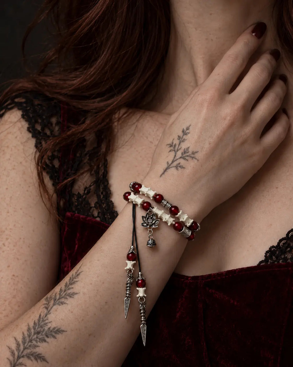 Crimson Lotus snake bone bracelet worn with the hand near the neck above a burgundy velvet neckline