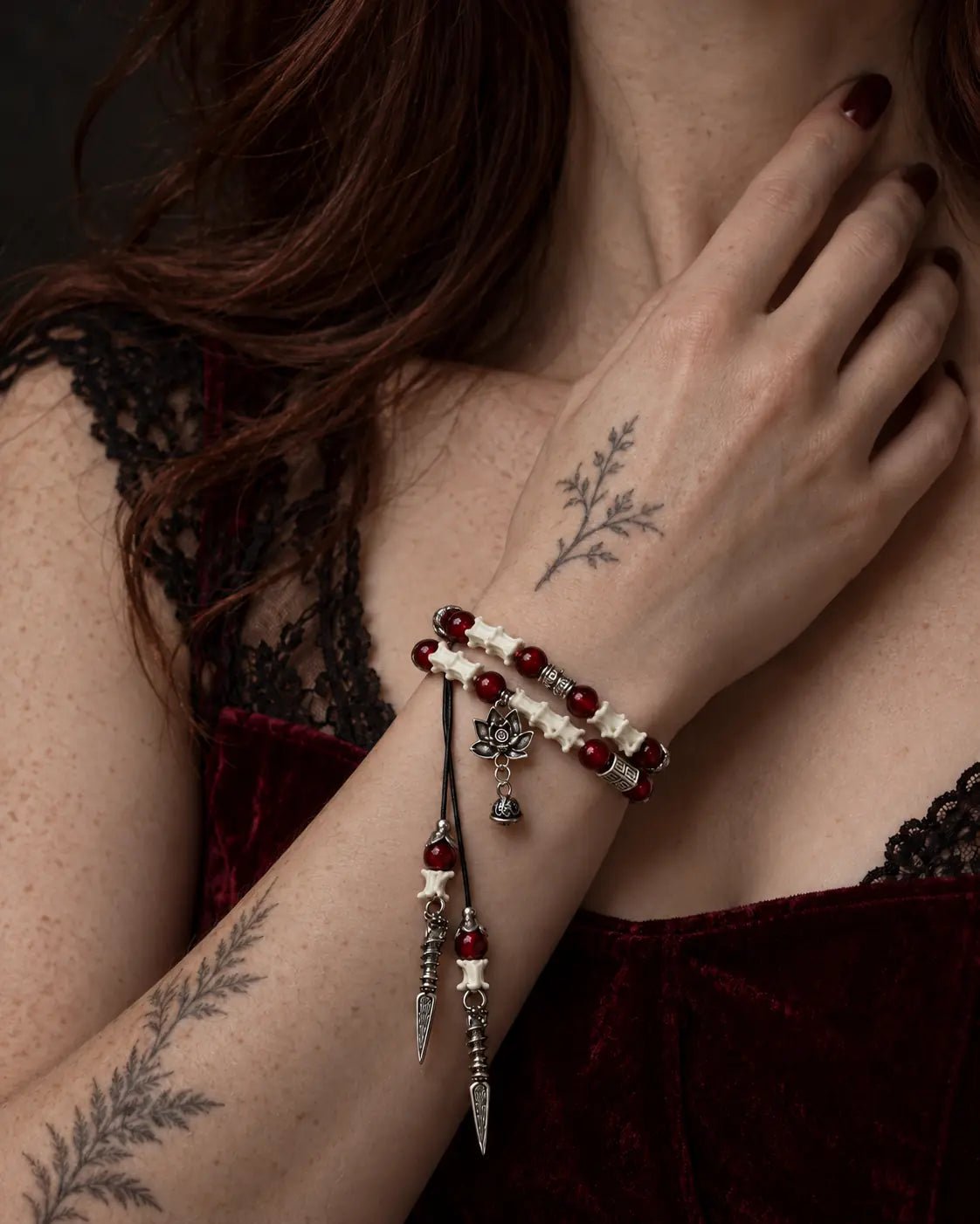 Crimson Lotus snake bone bracelet worn with the hand near the neck above a burgundy velvet neckline