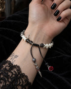 Palm-up view of the Crimson Rose snake bone bracelet showing its black sliding knot and rose- and pendant-tipped cords