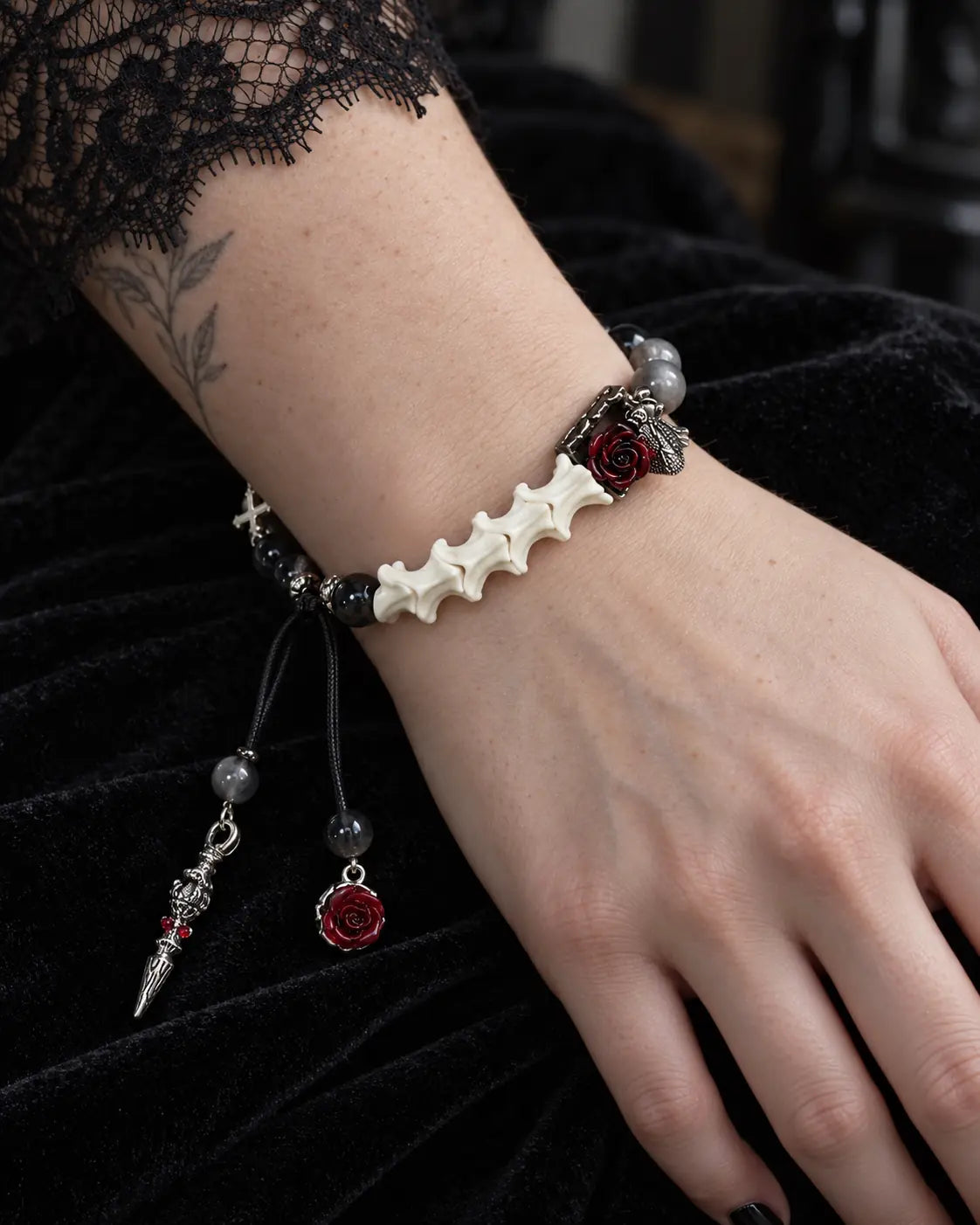 Crimson Rose snake bone bracelet on a hand resting on black velvet, showing white vertebrae beside a dark red rose