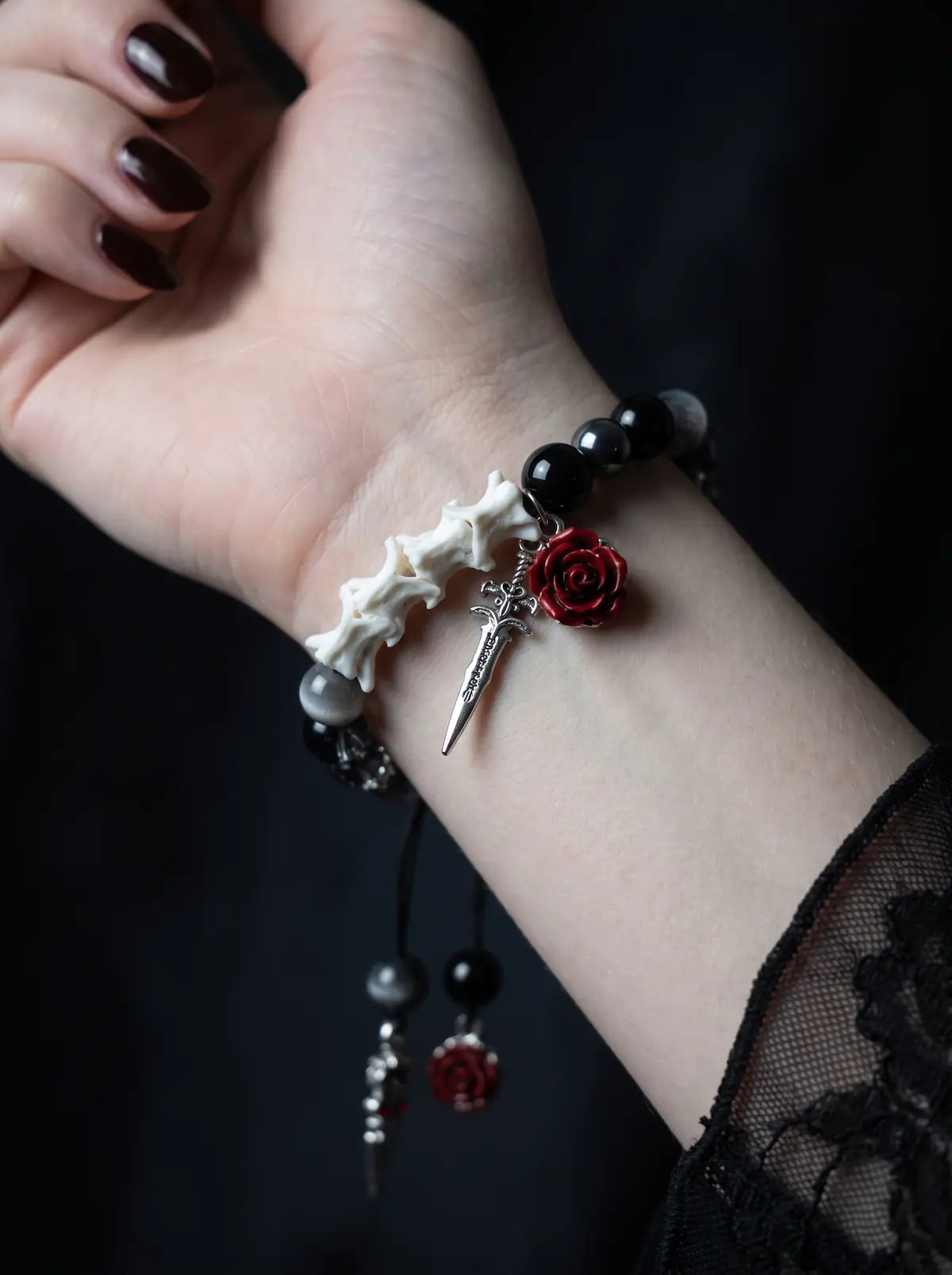Close-up of the Crimson Rose snake bone bracelet on the inner wrist, showing a red rose and silver-tone sword charm