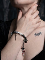 Crimson Rose snake bone bracelet worn with the hand at the neck above a black neckline, showing its sword and cross charms