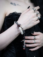 Crimson Rose snake bone bracelet worn with a ringed hand raised above a black corset, with its long cord ends hanging down