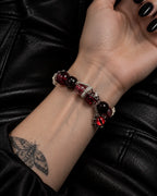 Palm-up close-up of the Crimson Serpent Eye snake bone bracelet showing red beads, a coiled serpent and the eye charm