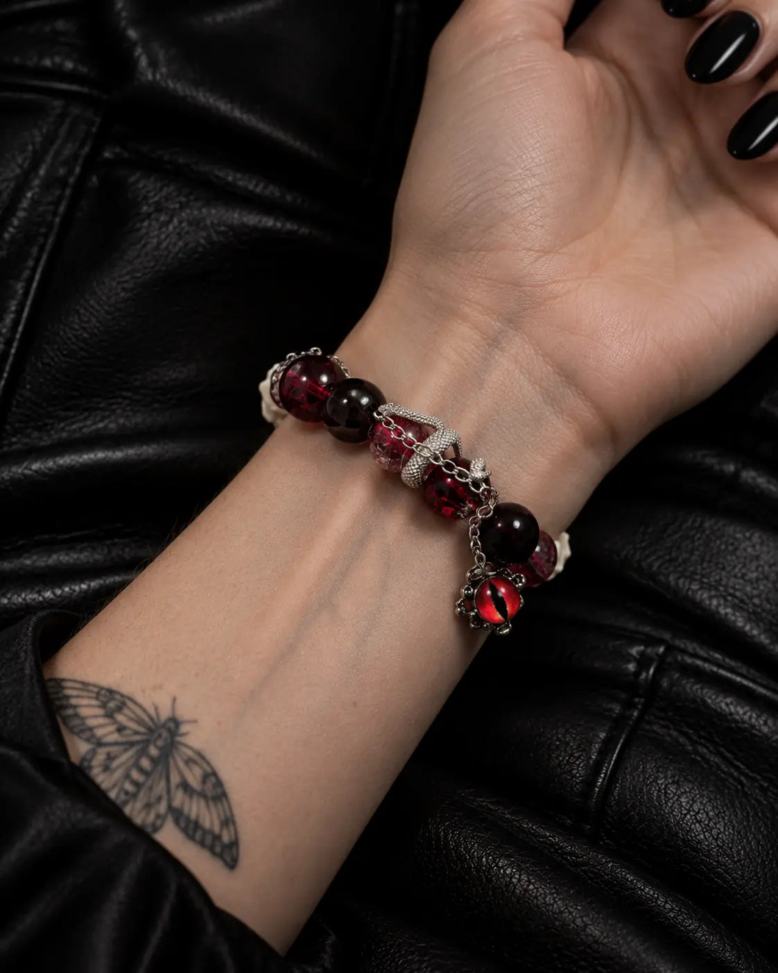 Palm-up close-up of the Crimson Serpent Eye snake bone bracelet showing red beads, a coiled serpent and the eye charm