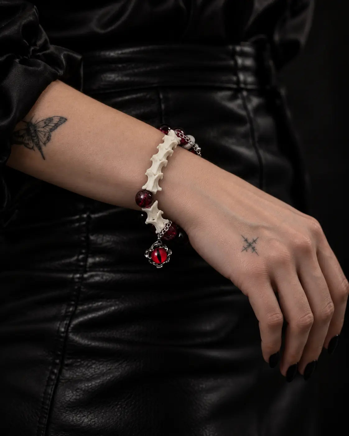 Side view of the Crimson Serpent Eye snake bone bracelet on a wrist across the lap, showing vertebrae and a red eye charm
