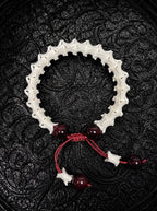 Crimson Spine snake bone bracelet with dark red beads, a red sliding knot and bone-tipped red cords on black fabric