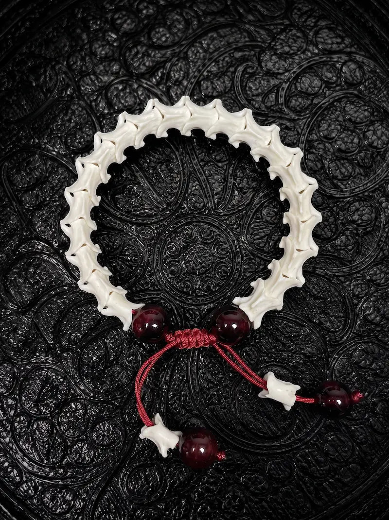 Crimson Spine snake bone bracelet with dark red beads, a red sliding knot and bone-tipped red cords on black fabric