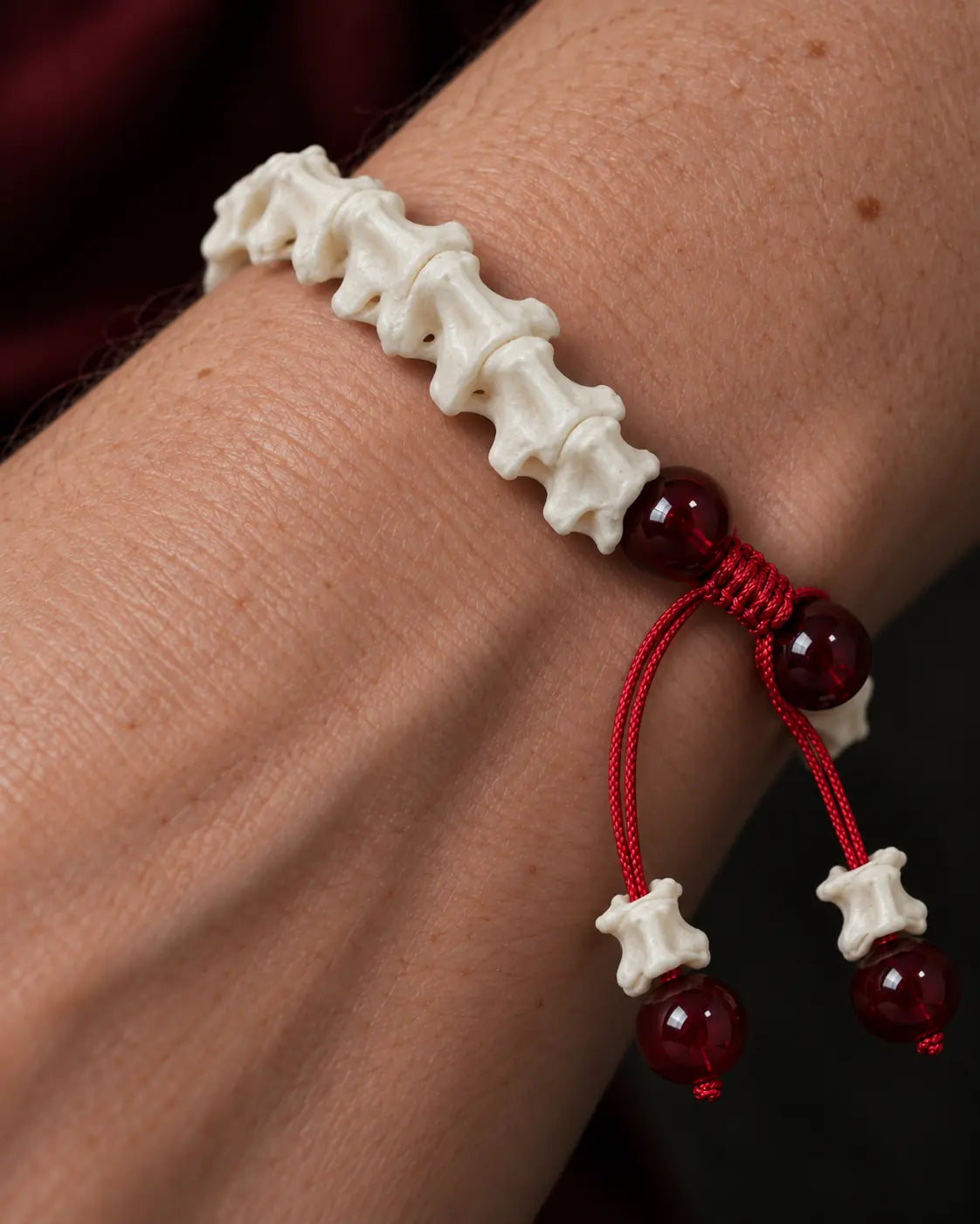 Close-up of the Crimson Spine snake bone bracelet showing white vertebrae, red beads and a red sliding knot