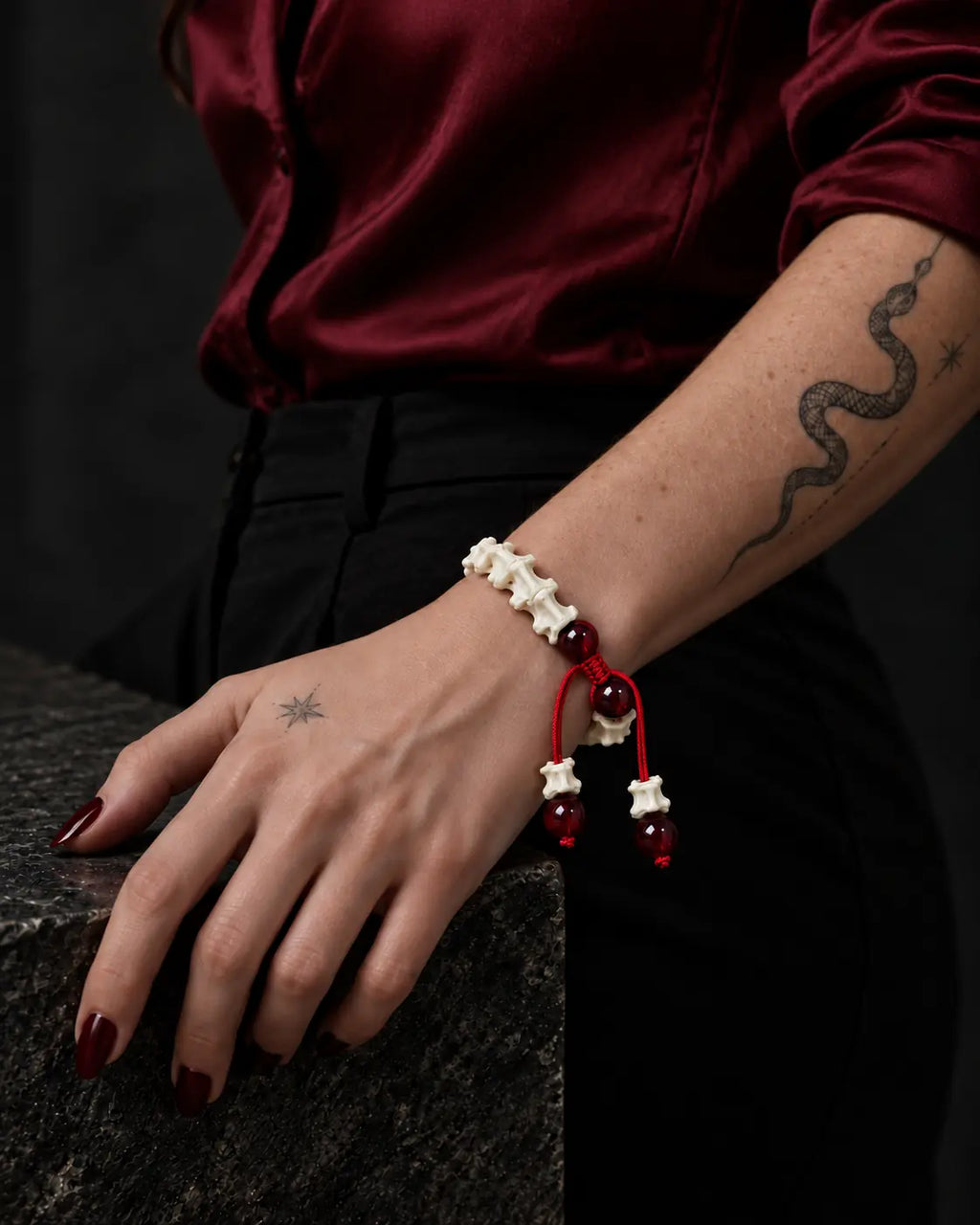 Crimson Spine snake bone bracelet on a wrist resting over a dark chair edge beneath a burgundy satin sleeve