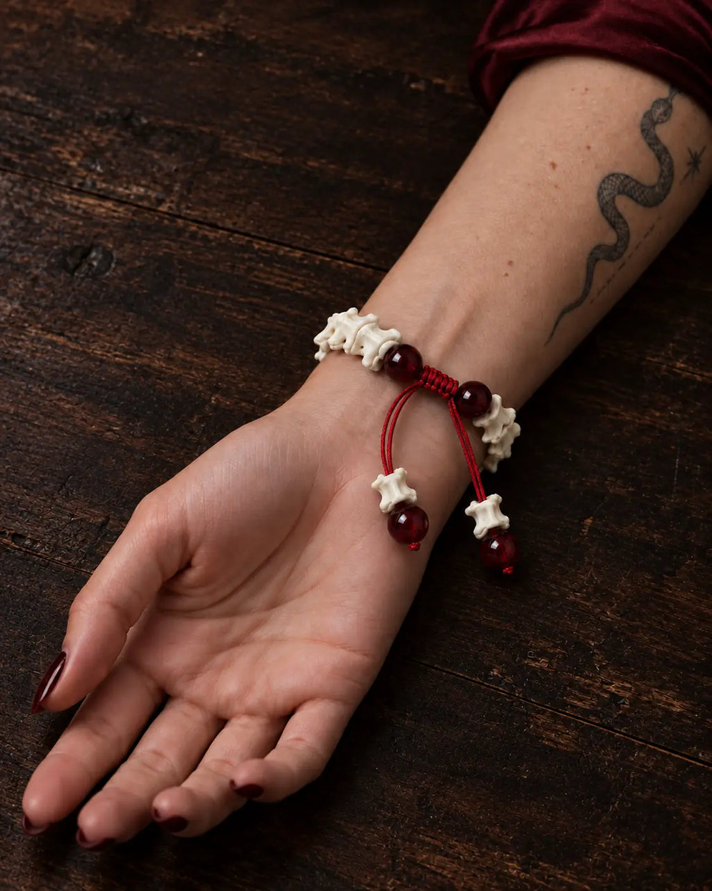 Palm-up view of the Crimson Spine snake bone bracelet on a wooden table, showing red cords and bead-tipped ends