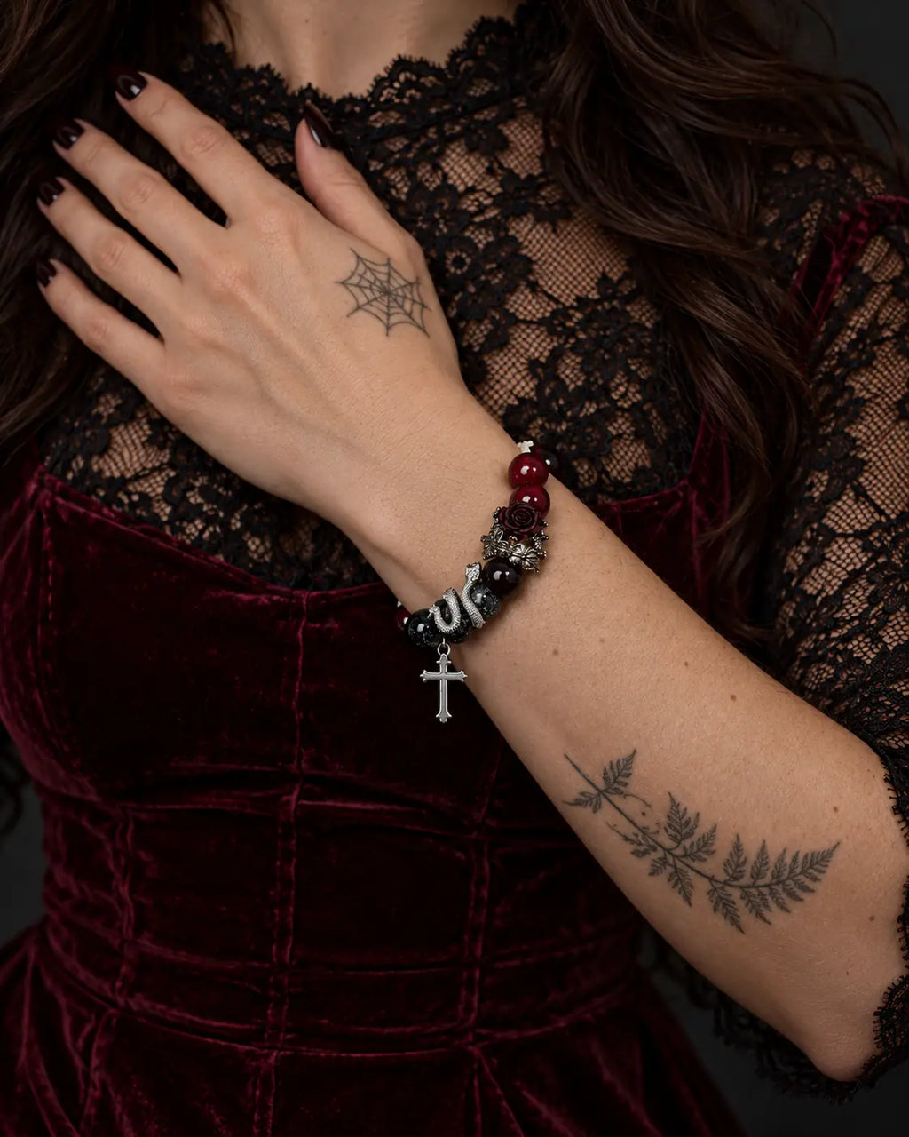Crimson Thorn snake bone bracelet worn with the hand against a black lace neckline above burgundy velvet