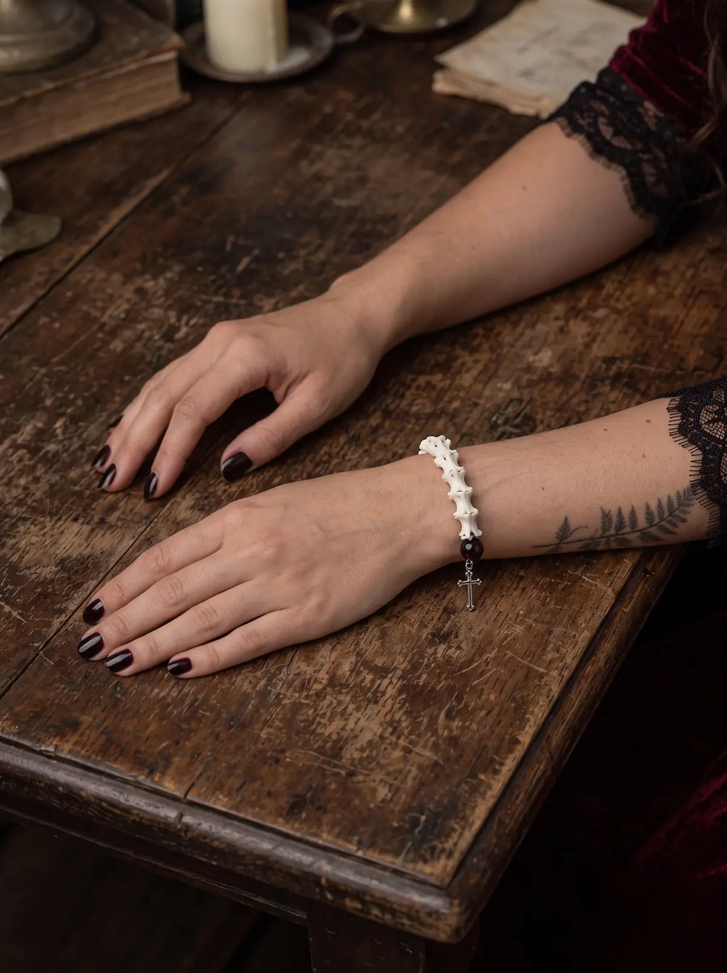 Crimson Thorn snake bone bracelet shown from the bone side with both hands resting on a worn wooden table