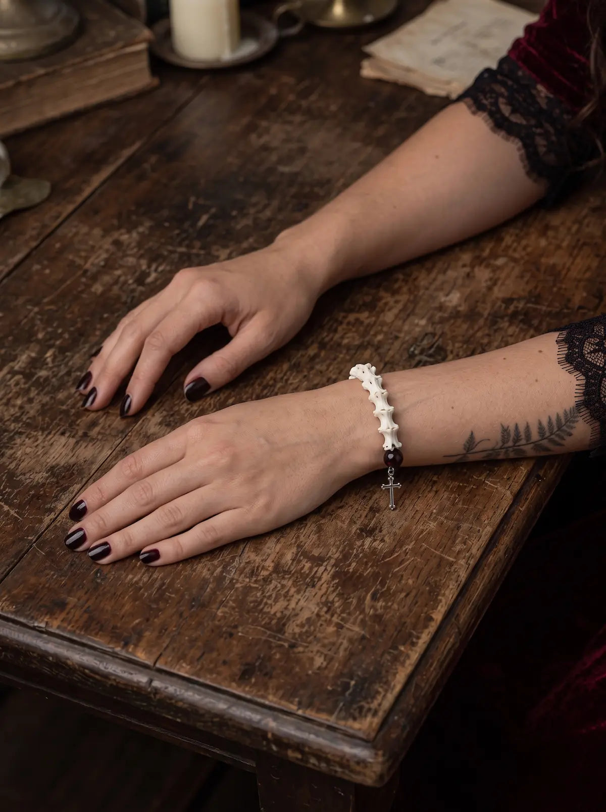 Crimson Thorn snake bone bracelet shown from the bone side with both hands resting on a worn wooden table