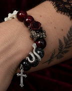Close-up of the Crimson Thorn snake bone bracelet showing a dark rose, coiled serpent and hanging silver-tone cross