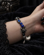 Duskdrake Snake Bone Bracelet, blue-bead and snake bone bracelet worn on a bent wrist over black fabric