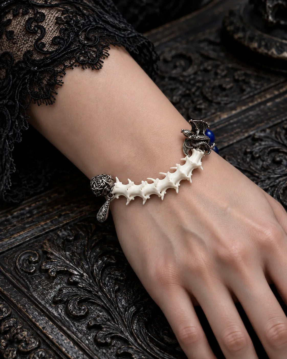 Duskdrake Snake Bone Bracelet, pale snake bone segment on the wrist beside an engraved dark tabletop