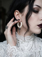 Ebon Thorn snake bone hoop earring worn above white lace with a hand touching the ear