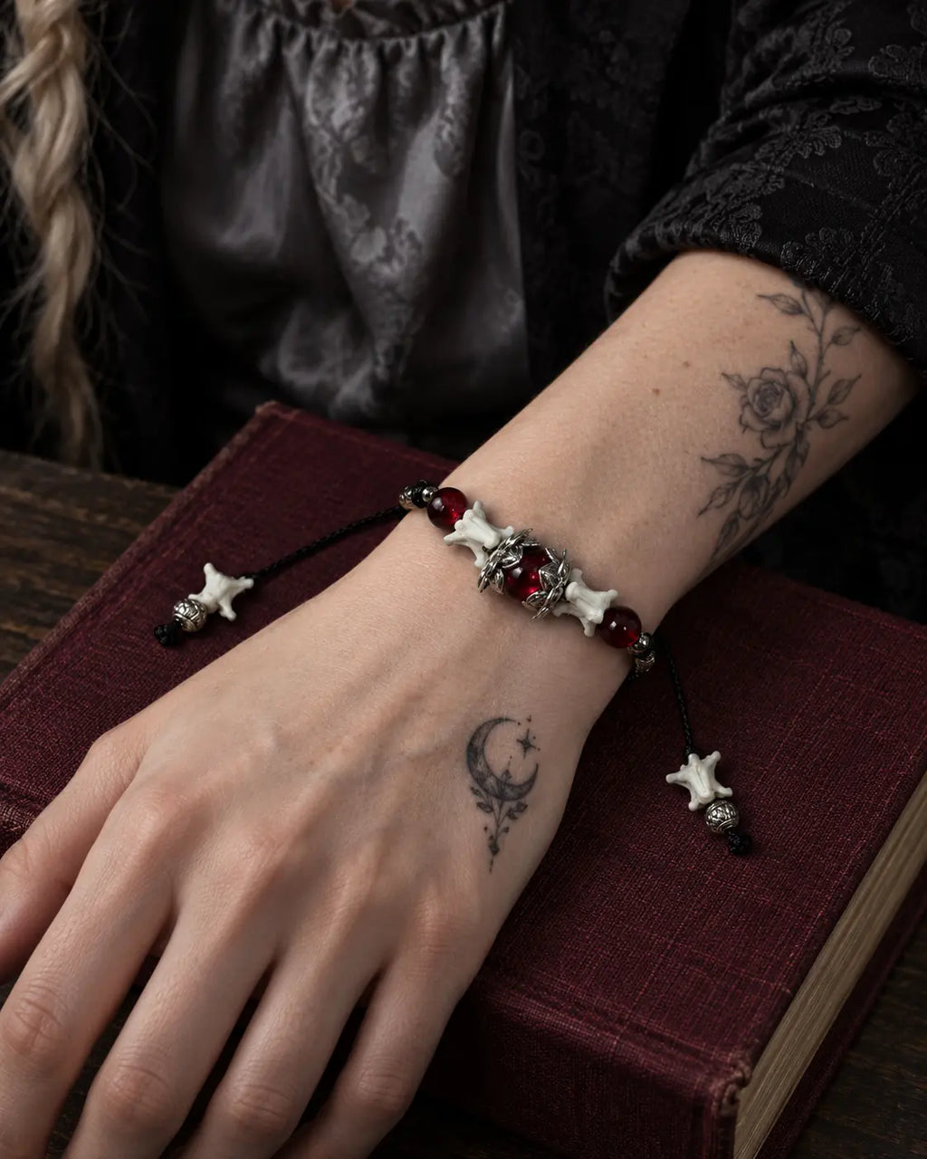Ember Bloom snake bone bracelet on a wrist resting across a burgundy book on a wooden table