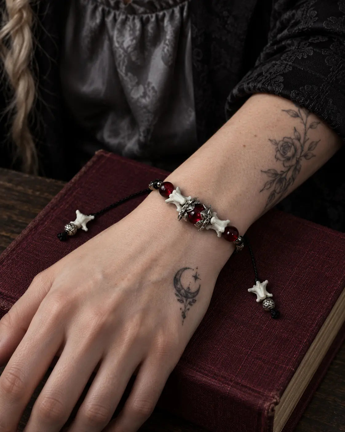 Ember Bloom snake bone bracelet on a wrist resting across a burgundy book on a wooden table