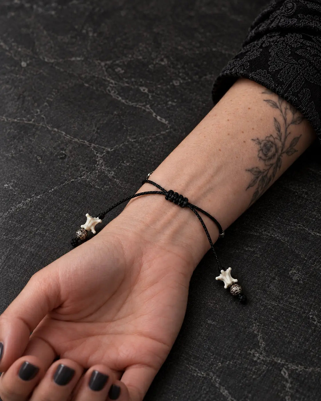 Palm-up view of the Ember Bloom snake bone bracelet showing its slim black braided closure and bone-tipped cords
