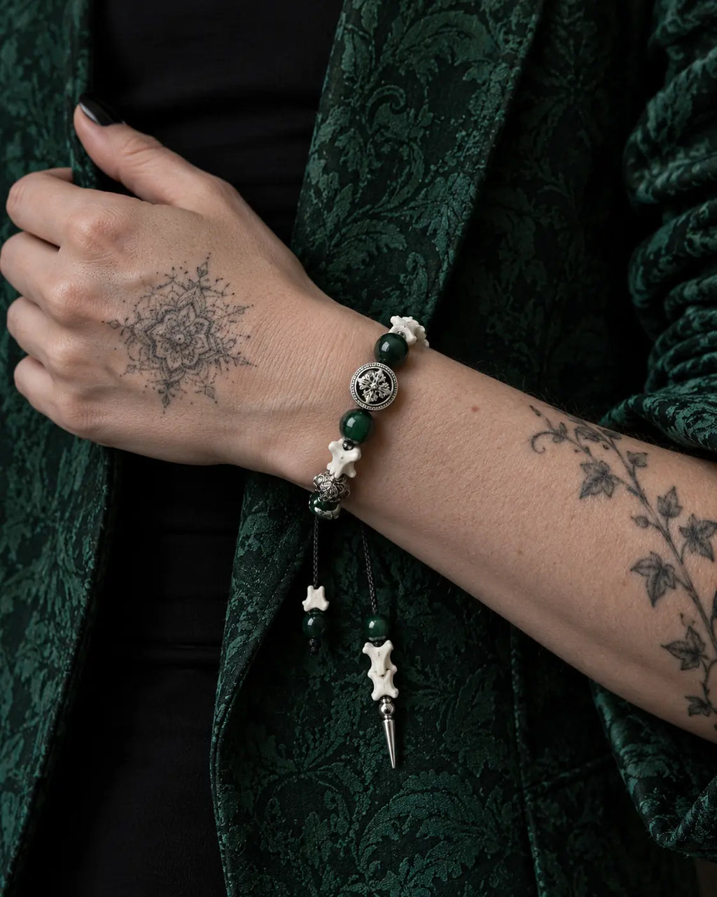 Emerald Thorn snake bone bracelet worn with the hand holding a green brocade jacket lapel