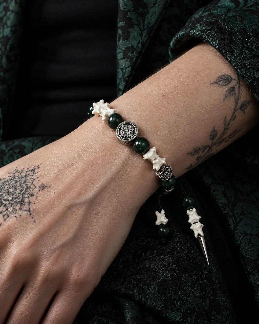 Close-up of the Emerald Thorn snake bone bracelet showing green beads and a round floral metal accent on the wrist
