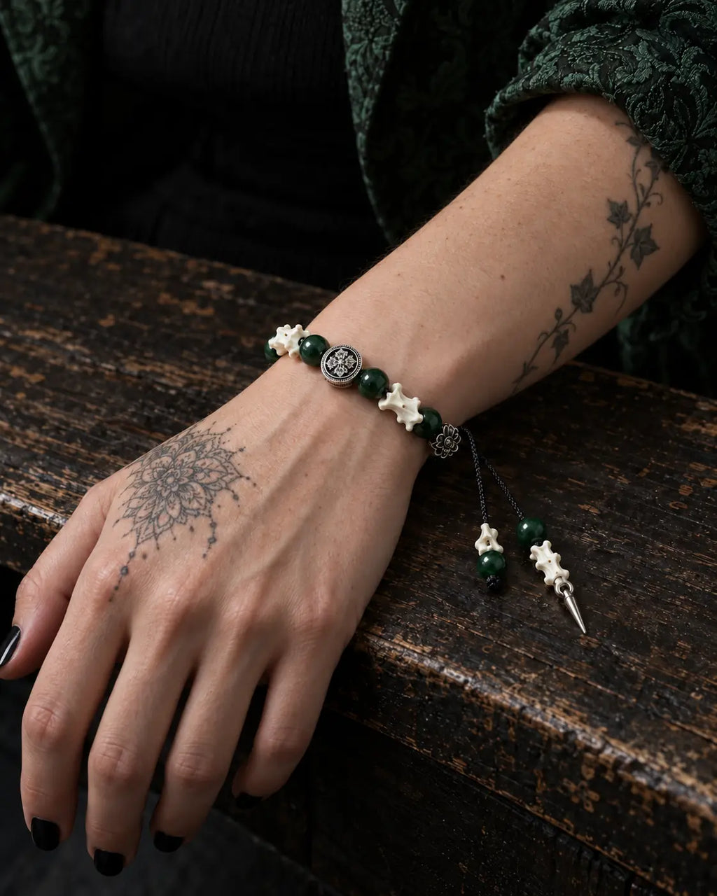 Emerald Thorn snake bone bracelet on a hand resting over the edge of a worn wooden table