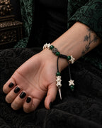 Palm-up view of the Emerald Thorn snake bone bracelet showing the sliding knot, green beads and pointed drop