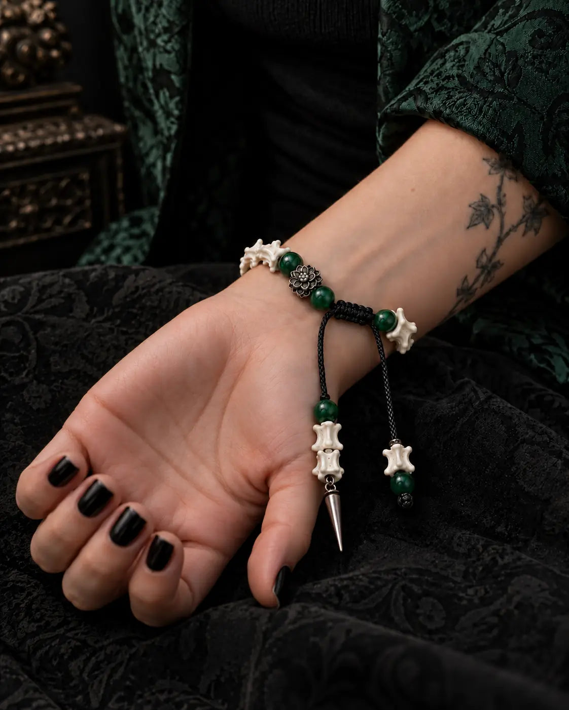 Palm-up view of the Emerald Thorn snake bone bracelet showing the sliding knot, green beads and pointed drop