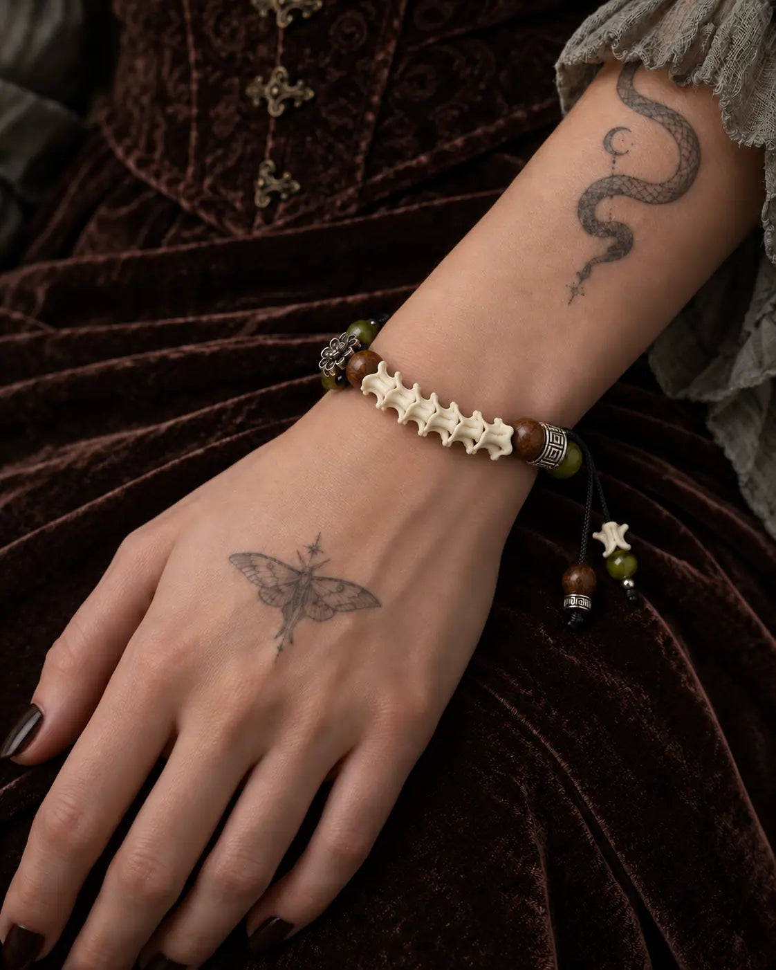 Forest Bloom snake bone bracelet worn on a wrist resting against brown velvet