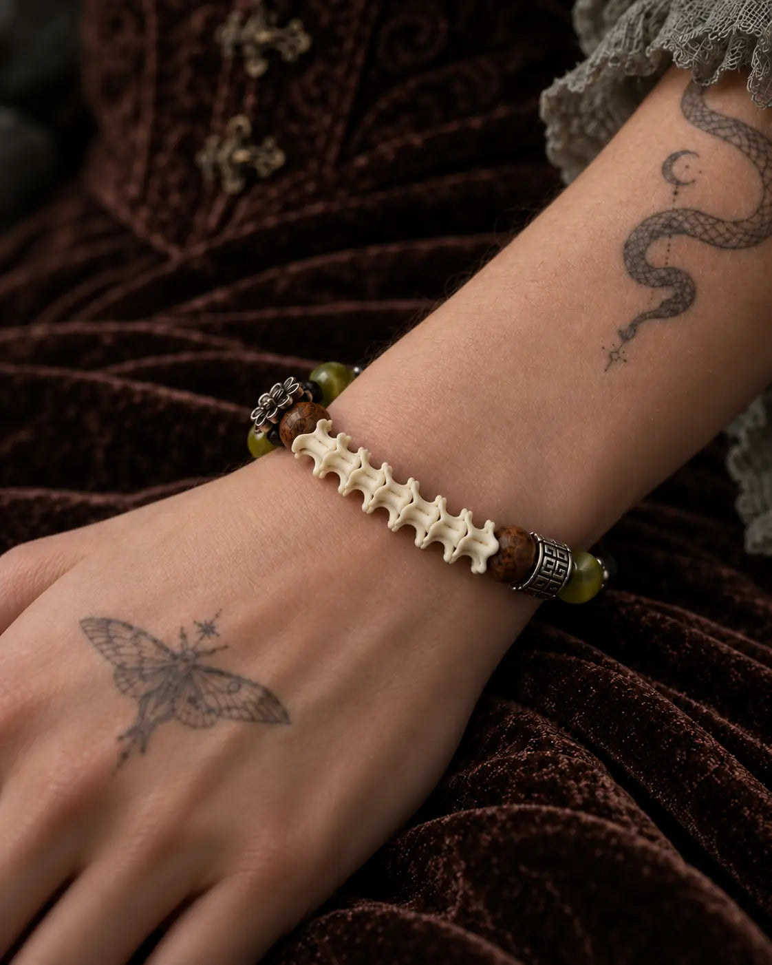 Close-up of the Forest Bloom snake bone bracelet showing white vertebrae and engraved metal spacers on the wrist