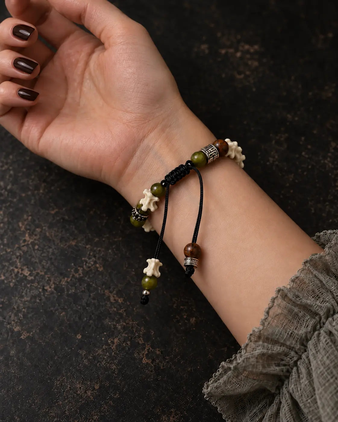 Palm-up view of the Forest Bloom snake bone bracelet showing the sliding knot and dangling green and brown beads