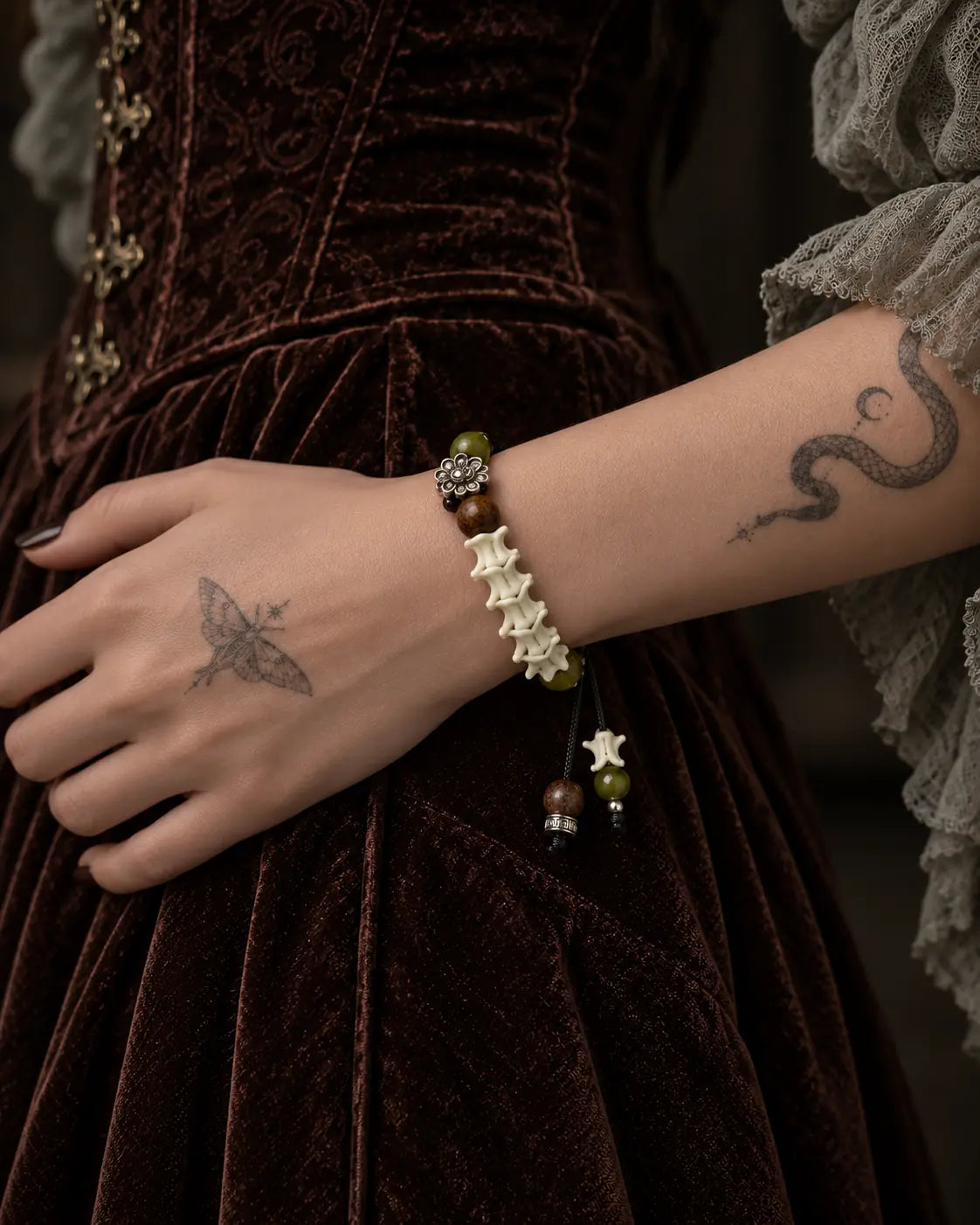 Side view of the Forest Bloom snake bone bracelet across a wrist against a brown velvet dress