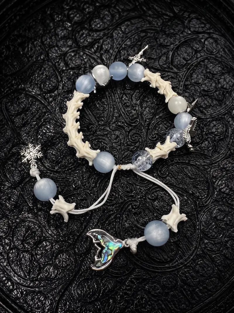 Frost Tide snake bone bracelet with pale blue beads, a snowflake charm and an iridescent tail pendant on white cords