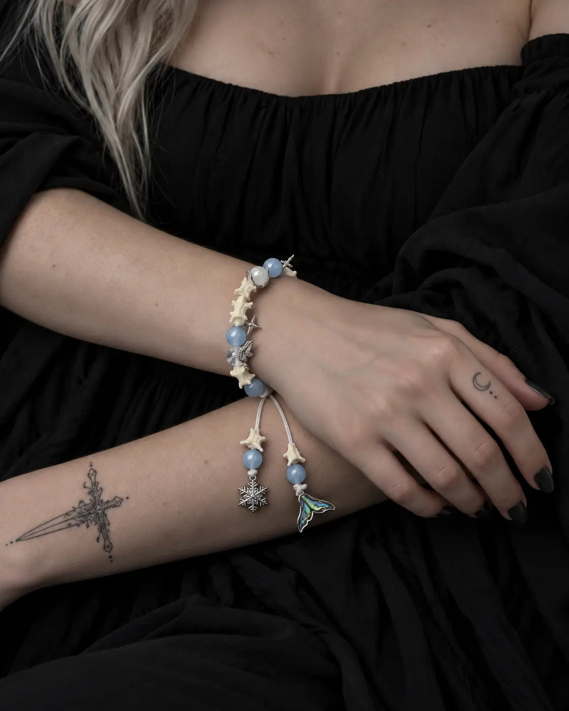 Frost Tide snake bone bracelet worn across folded arms, showing the snowflake and shimmering tail drops