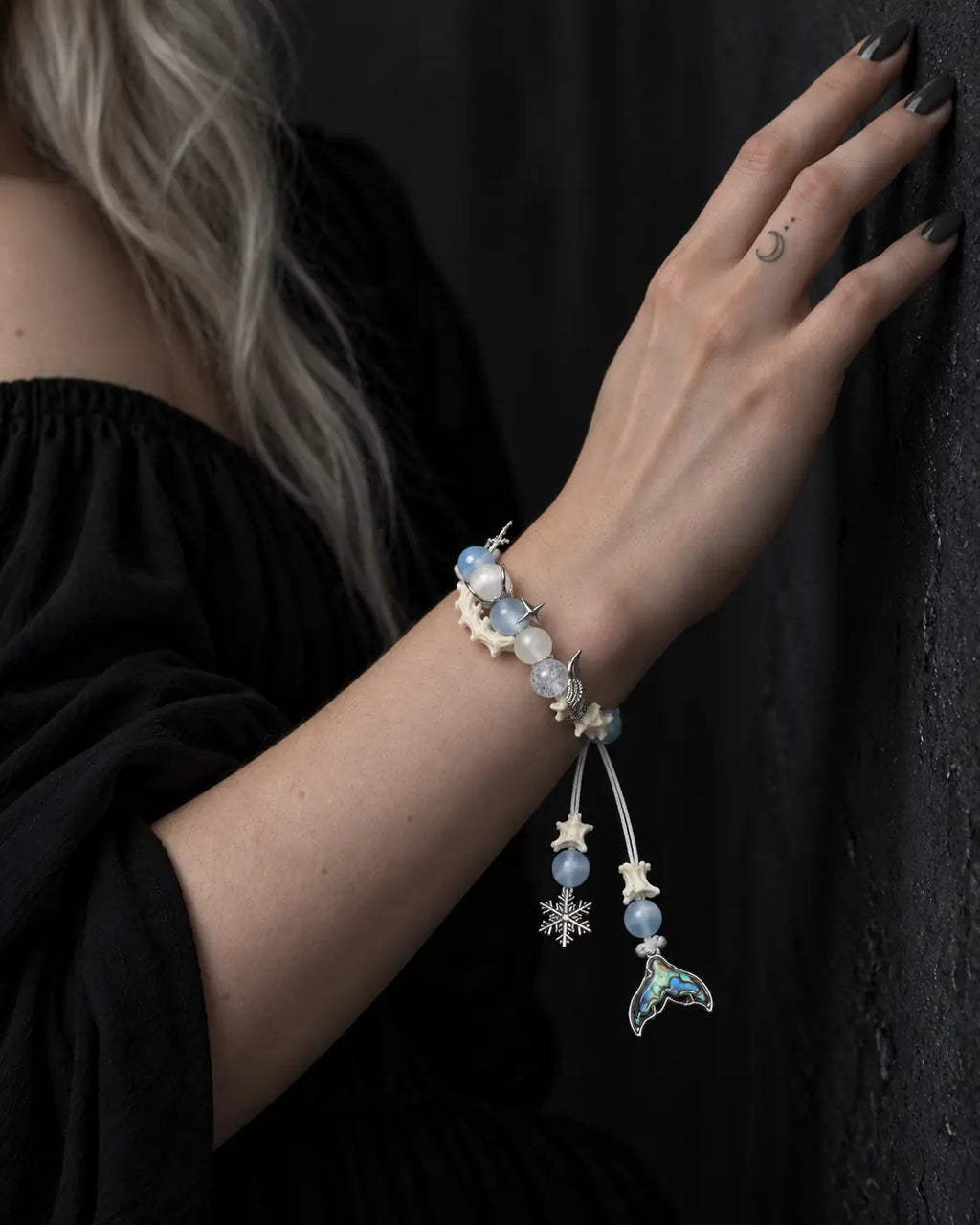Frost Tide snake bone bracelet on a raised wrist beside a dark wall, with its two charms hanging down