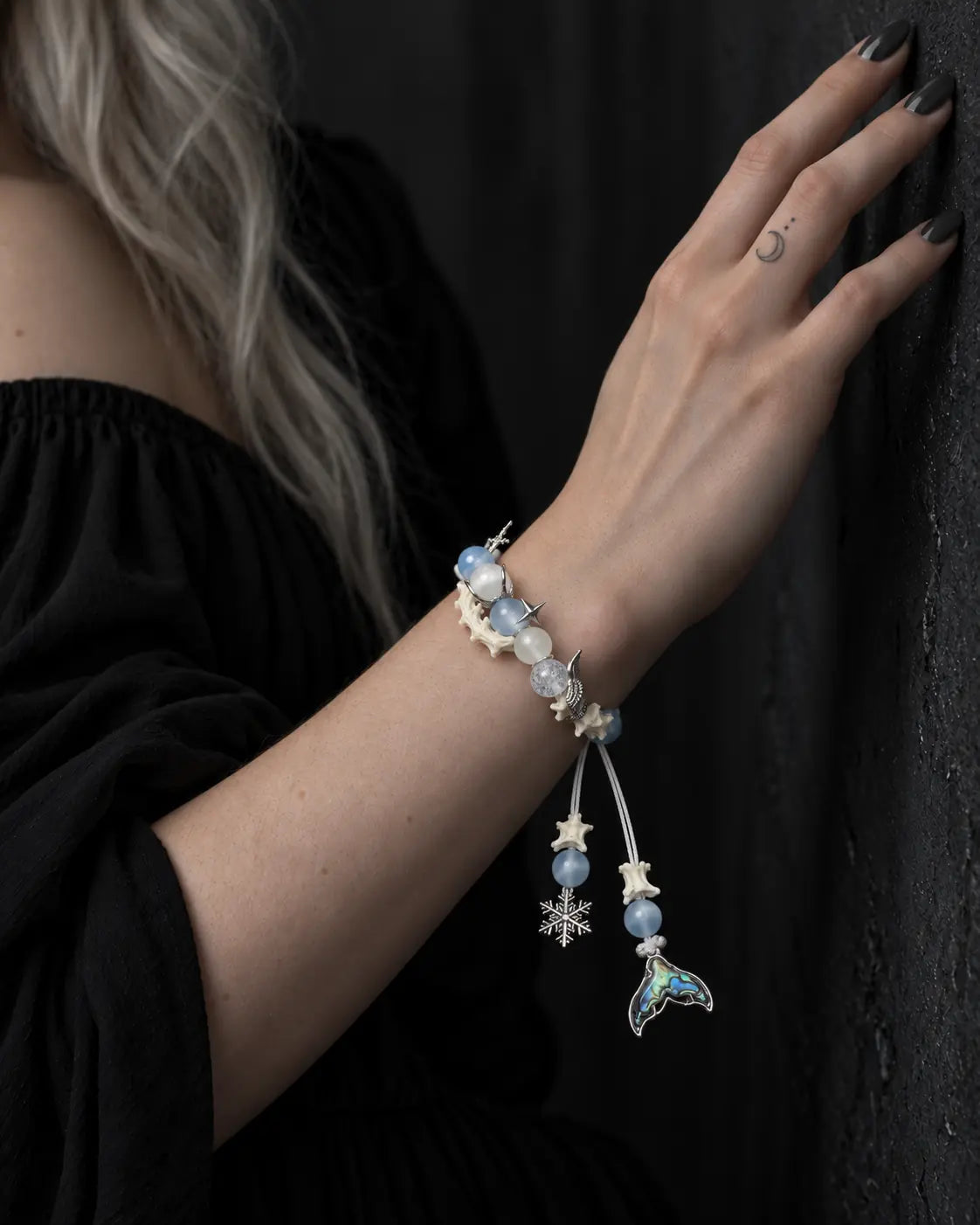 Frost Tide snake bone bracelet on a raised wrist beside a dark wall, with its two charms hanging down