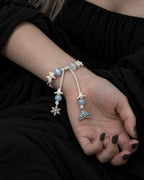 Palm-up view of the Frost Tide snake bone bracelet showing its white sliding knot, snowflake and iridescent tail charms